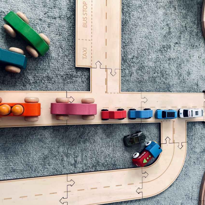 Wooden road track set with different coloured cars on a green grey carpet background, showing the different car sizes in comparison to the timber towns road tracks
